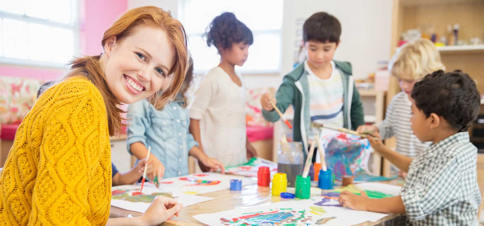 Leerkracht primair onderwijs helpt kinderen bij schilderles